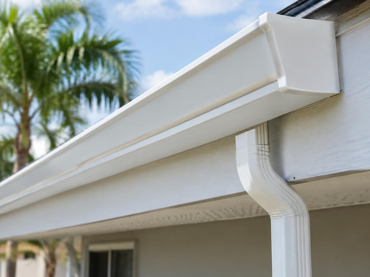 Close-up of a white aluminum gutter with hidden hangers and a downspout outlet on a fascia board