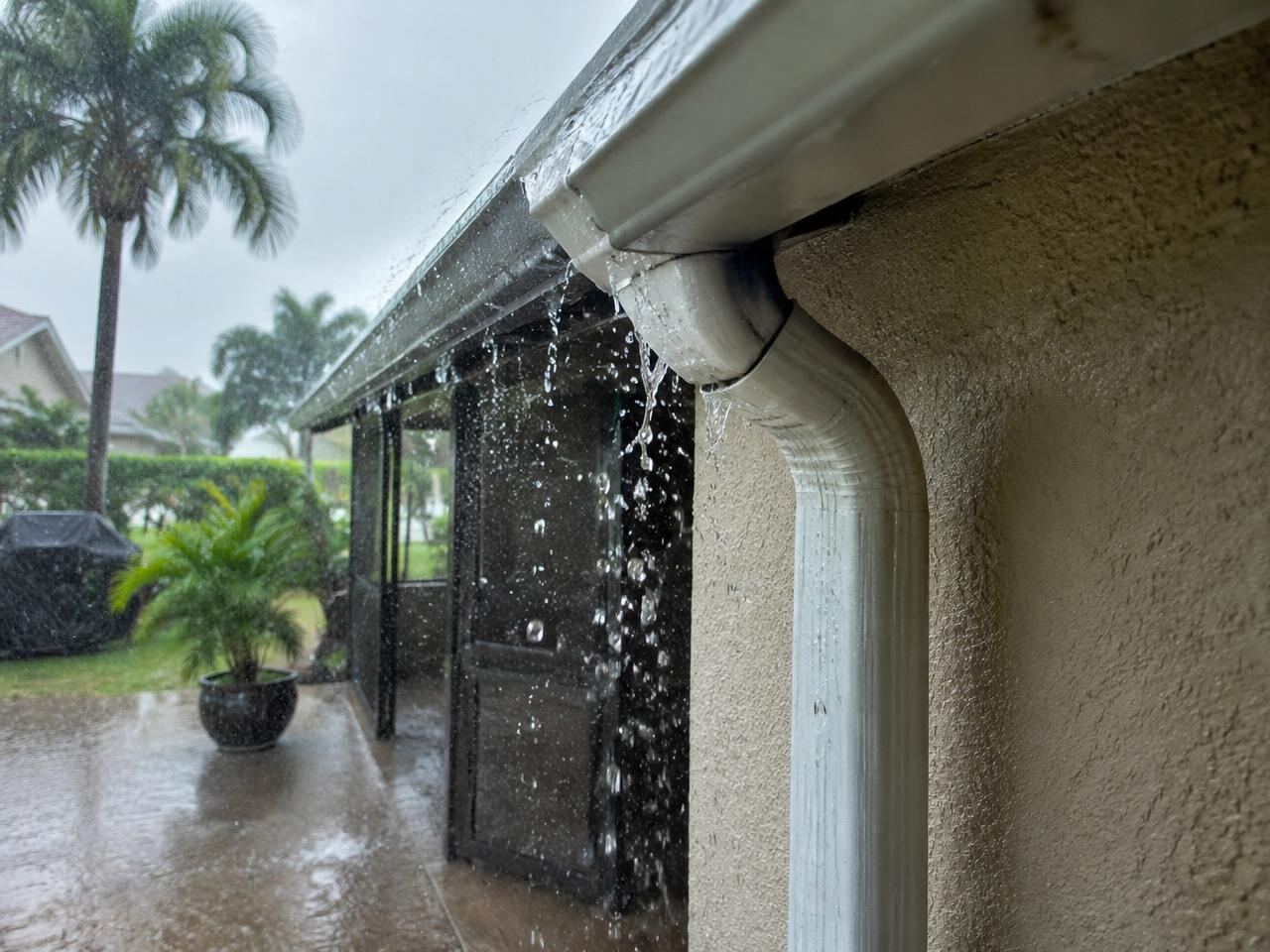Rainwater spilling from a leaking gutter joint onto a patio during a Florida storm